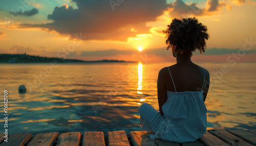 A young girl sits on a dock by the ocean, looking out at the sunset photo