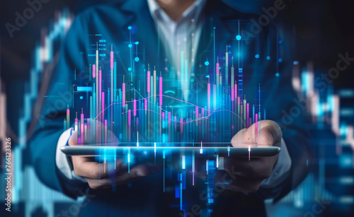 A businessman holding a tablet displaying a digital stock market graph and chart in the style of financial growth on a blue background.  photo