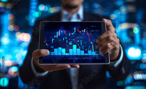 A businessman holding a tablet displaying a digital stock market graph and chart in the style of financial growth on a blue background. 