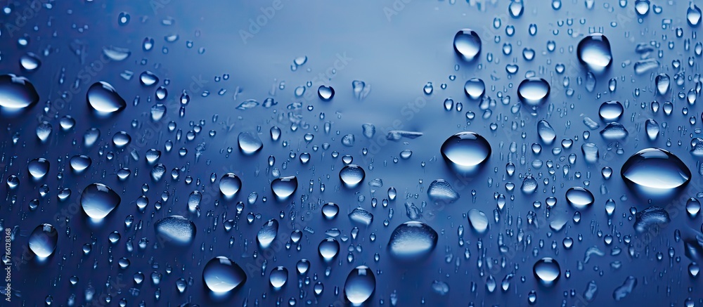 A multitude of liquid droplets rest on an azure surface, resembling a drizzle or dew. The electric blue hue of the water drops adds a touch of vibrancy