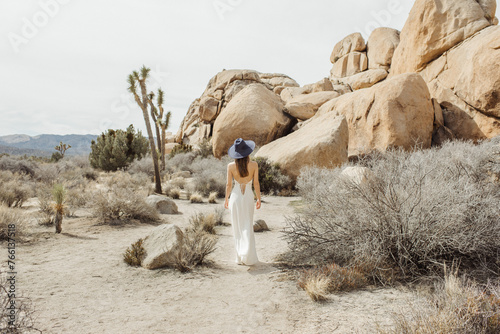 Woman in a boho style white dress and hat walking in the Joshua Tree desert 