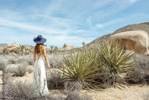 Woman in a boho style white dress and hat standing near wild plants in the Joshua Tree desert