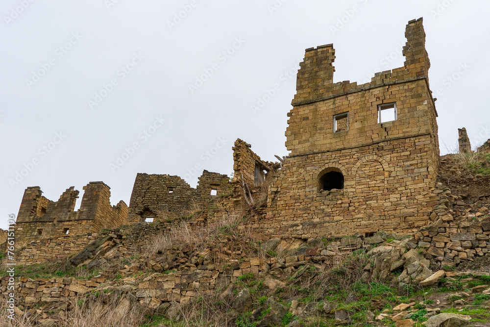 Ruins of ancient settlement in mountains. Ruined mountainous village Gamsutl in Dagestan republic. Old abandoned stone houses and buildings against spring landscape. Caucasian aul, Caucasus, Russia