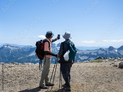 Hikers taking selfie photos using a smartphone at Skyline Trail. Plastic bag with rubbish on backpack. Take your garbage home concept. Mt Rainier National Park. Washington State.