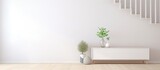 A simple, elegant white dresser is paired with a lush green plant in a spacious, well-lit white room