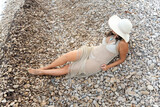 Elegant curvy girl with hat lying on the rocks on the beach.