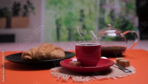 Tazzina di caffè fumante, colazione con cornetto e caffè, tavola con sfondo arancione photo