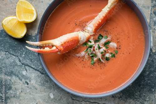 Plate of bisque served with a boiled crab claw, horizontal shot on a grey and beige granite surface, middle closeup, flat lay