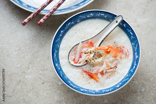 Bowl of asian congee or conjee with crab meat on a beige stone background, horizontal shot, elevated view