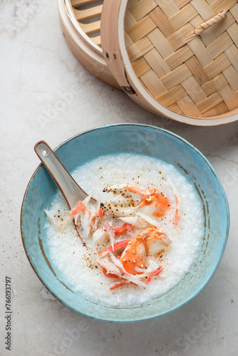 Turquoise bowl with crab congee or a type of panasian rice porridge, vertical shot on a light-beige stone background