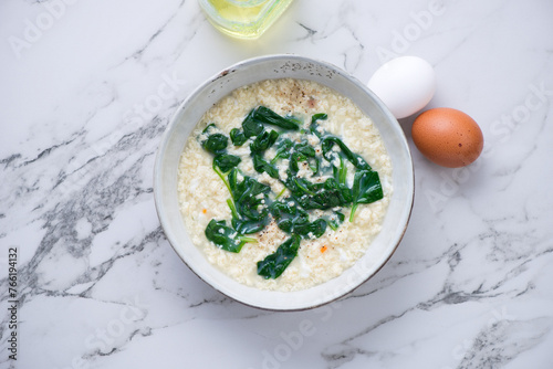 Bowl of italian stracciatella soup with spinach, flat lay on a white marble background, horizontal shot with space