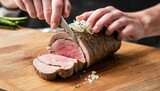 slicing a serving of organic roast beef roll with knife on wood table with garlic pepper and salt in melbourne australia