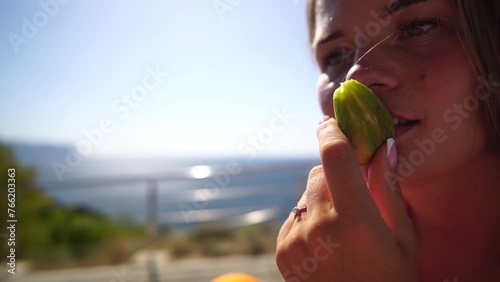 Woman smells fig. Fresh ripe fig fruit in the hands. A young woman eats figs on the beach, near sea. Ficus carica, Fig - green-yellow fruit. Close up. Slow motion photo