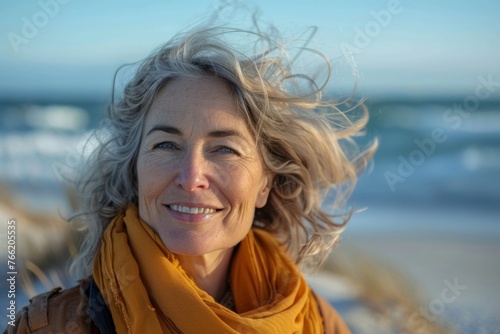 A mature woman is smiling on the beach, enjoying the natural and carefree lifestyle, soaking up the sunny and breezy weather, and taking in the fresh ocean breeze with joy. © tonstock