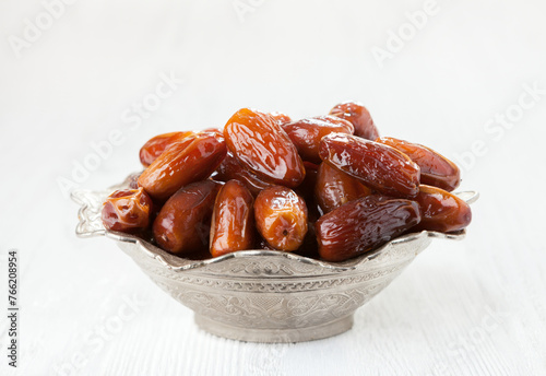 Bowl full of dates on a white wooden background.