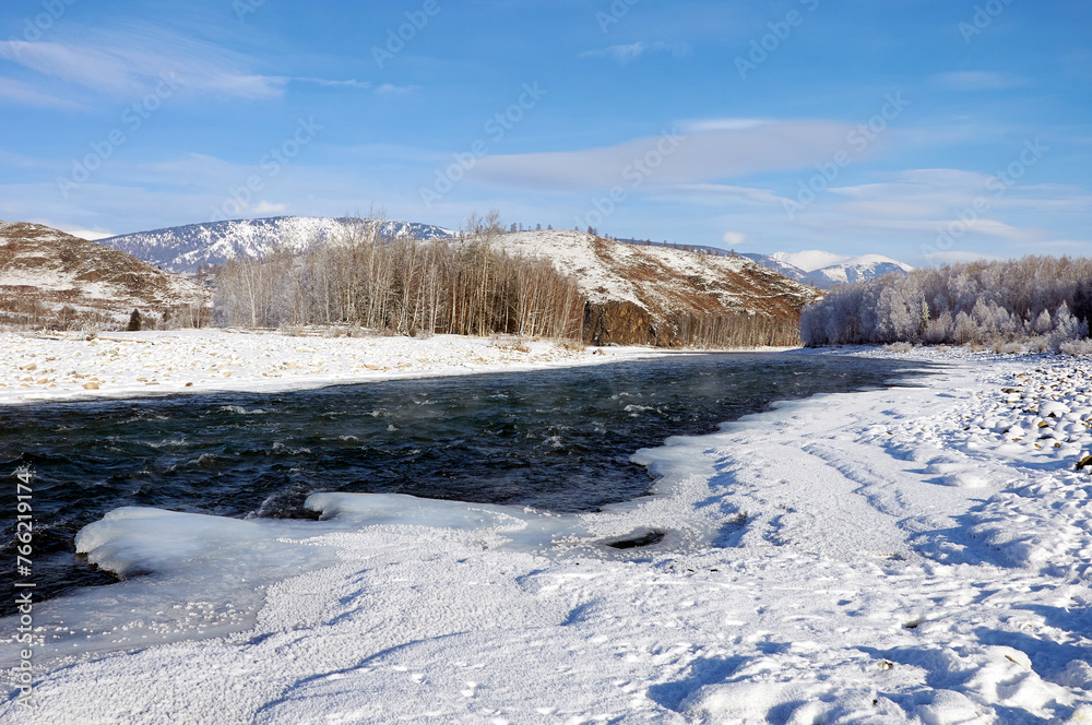 A frozen river bank with a distant mountain under a cloudy sky A frozen river bank with a distant mountain under a cloudy sky