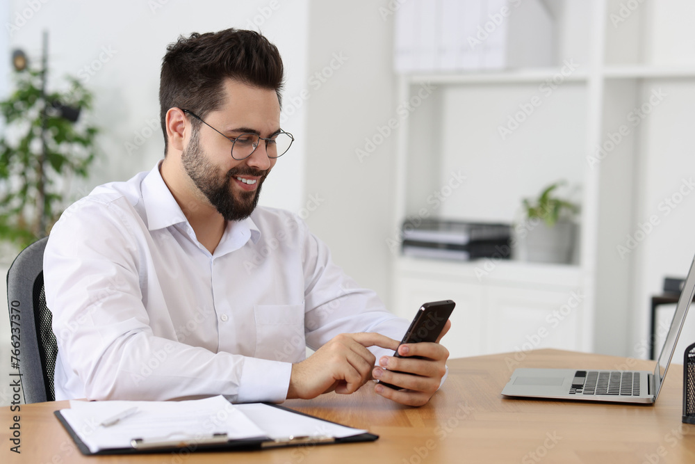 Handsome young man using smartphone at wooden table in office Handsome young man using smartphone at wooden table in office