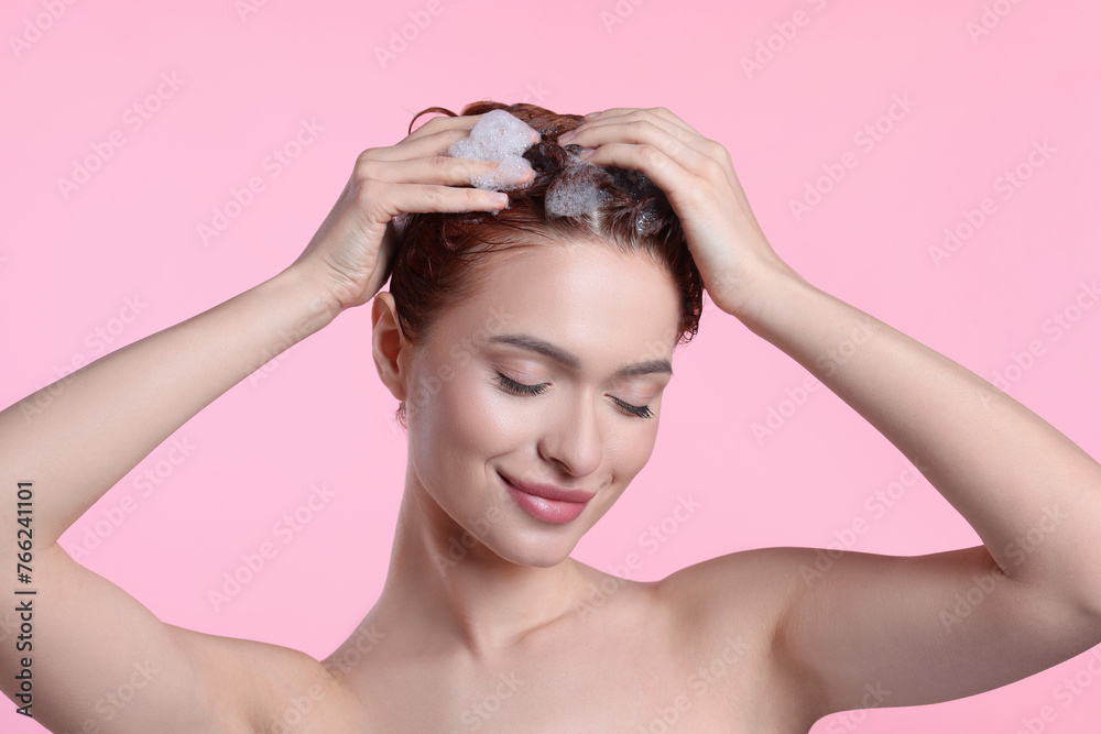 Happy young woman washing her hair with shampoo on pink background Happy young woman washing her hair with shampoo on pink background