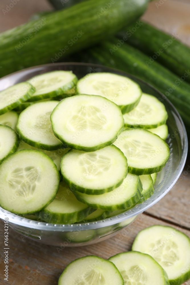 Cut cucumber in glass bowl and fresh vegetables on wooden table, closeup Cut cucumber in glass bowl and fresh vegetables on wooden table, closeup