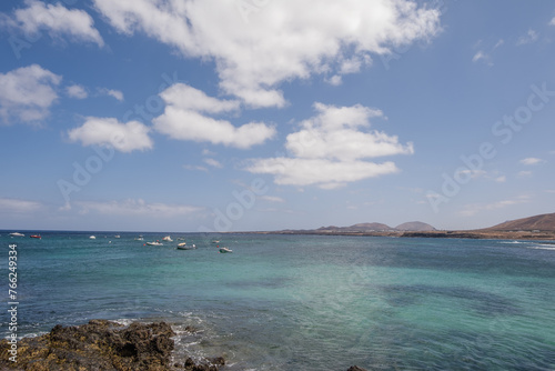 Seascape. Rocks in the foreground. Group of boats anchored nearby. Mountains in the background. Turquoise Atlantic Ocean. Big white clouds. Village of Arrieta. Lanzarote, Canary Islands, Spain photo