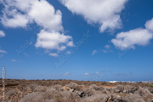 Deserted landscape on the outskirts of the village of Arrieta. Dry bushes, red earth and mountains in the background. Large white clouds. Village of Arrieta. Lanzarote, Canary Islands, Spain photo