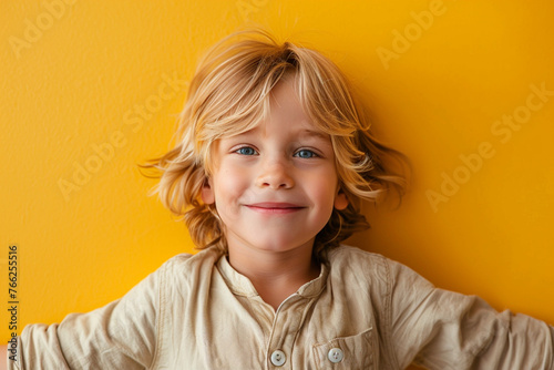 Little cute fun happy blond long-haired kid boy 5 years old wearing casual clothes posing isolated on bright yellow wall color background children studio portrait. People childhood lifestyle