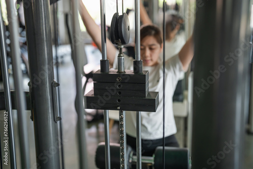 Asian sport woman working out on a weight machine at gym fitness. The machine is a multi-station weight machine with a barbell attached to it. The woman is lifting weights and focused on her workout.