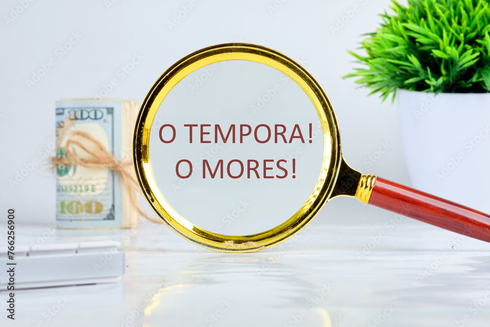 o tempora, o mores (O, the times O, the morals) Latin phrase through a magnifying glass on a gray background, a roll of banknotes and a green plant in the background - obrazy, fototapety, plakaty 