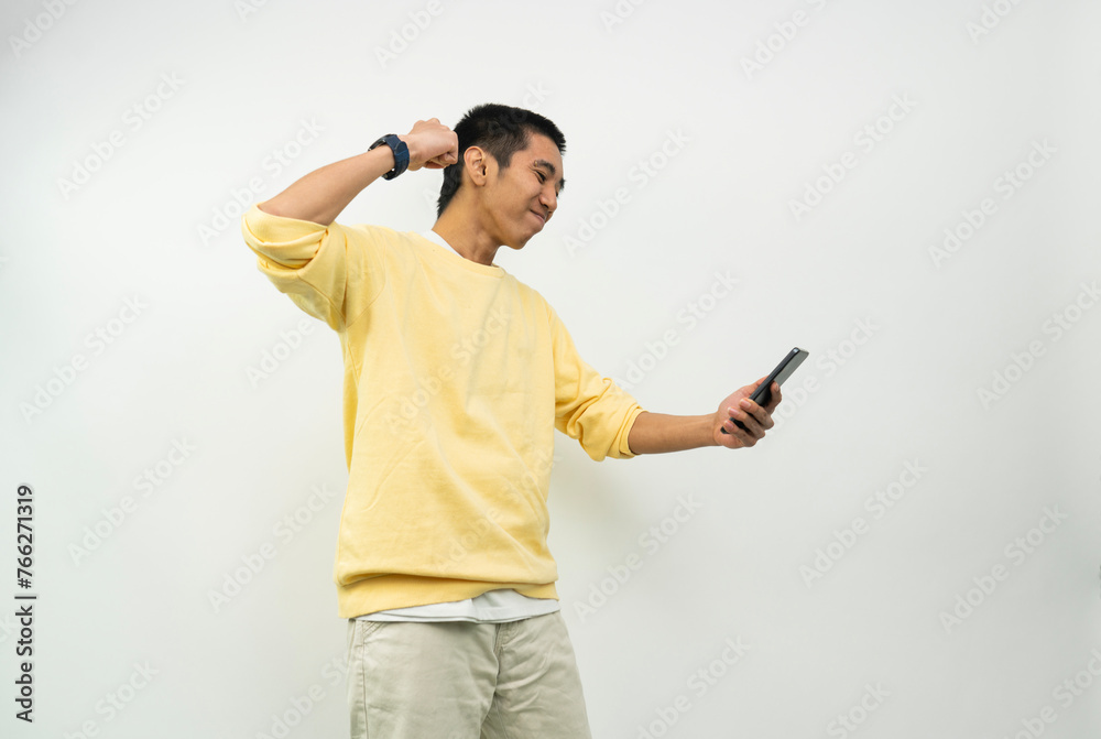 young man wearing a phone standing on a white background isolated with the proud phone and celebrating victory and success very excited while looking at the phone with a clenched fist. young man wearing a phone standing on a white background isolated with the proud phone and celebrating victory and success very excited while looking at the phone with a clenched fist.