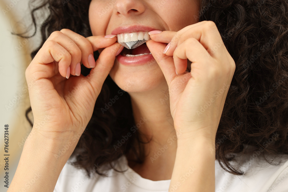 Young woman applying whitening strip on her teeth indoors, closeup Young woman applying whitening strip on her teeth indoors, closeup