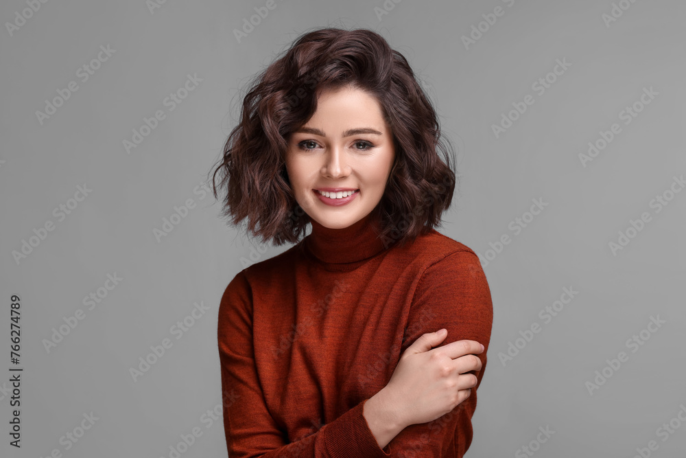 Fototapeta premium Portrait of beautiful young woman with wavy hairstyle on grey background. Space for text