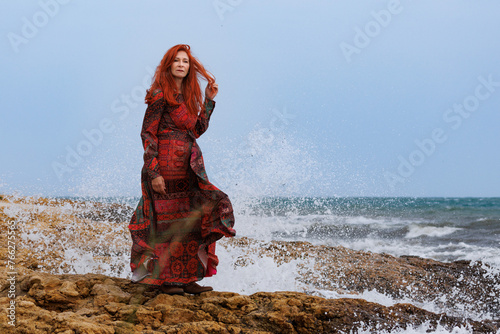 Mujer con vestido en la costa de rocas del mar mediterraneo durante temporal de levante con mucho viento, Santa Pola, España