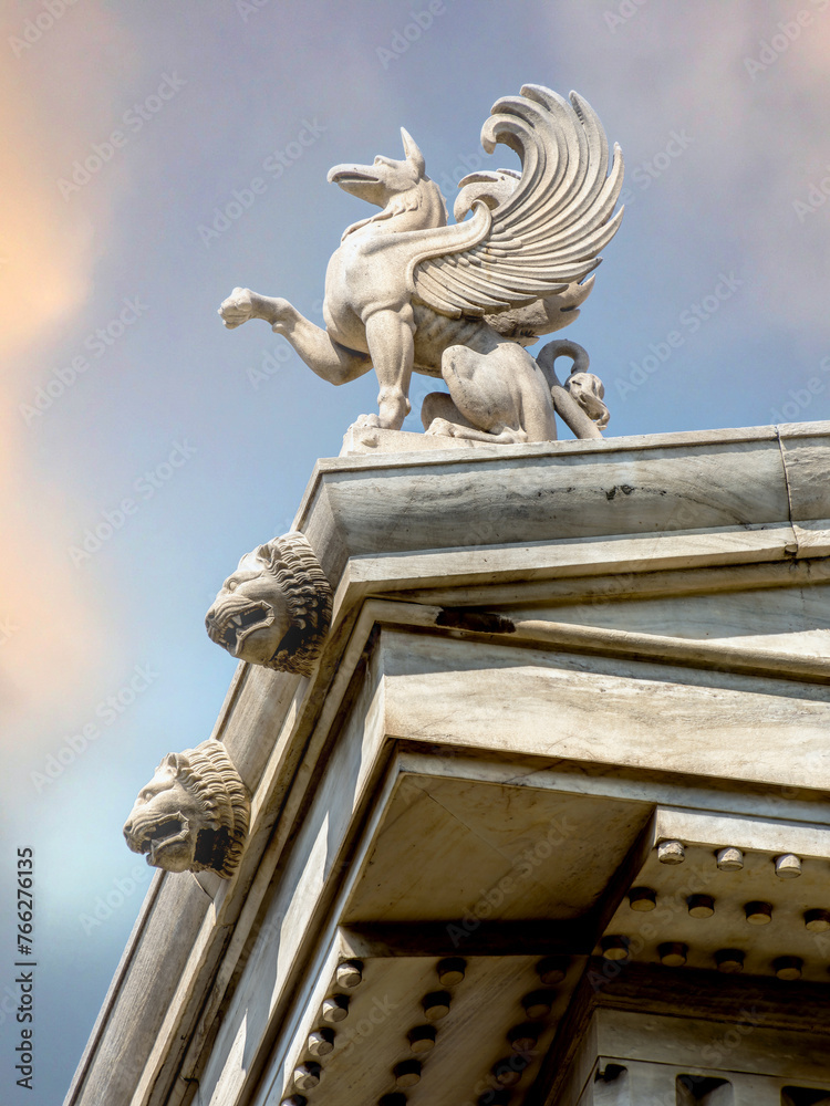 Obraz premium A Griffon statuette stands on the roof of Athens National University. Griffins were known for guarding treasures and priceless possessions. Cultural travel in Greece.