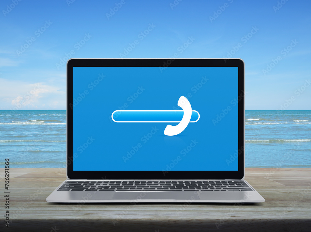 Phone icon with copy space for add your phone number on modern laptop computer monitor screen on wooden table over tropical sea and blue sky with white clouds, Business contact us concept