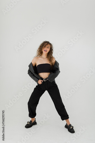 A young woman with curly hair and in black pants posing in light photostudio 