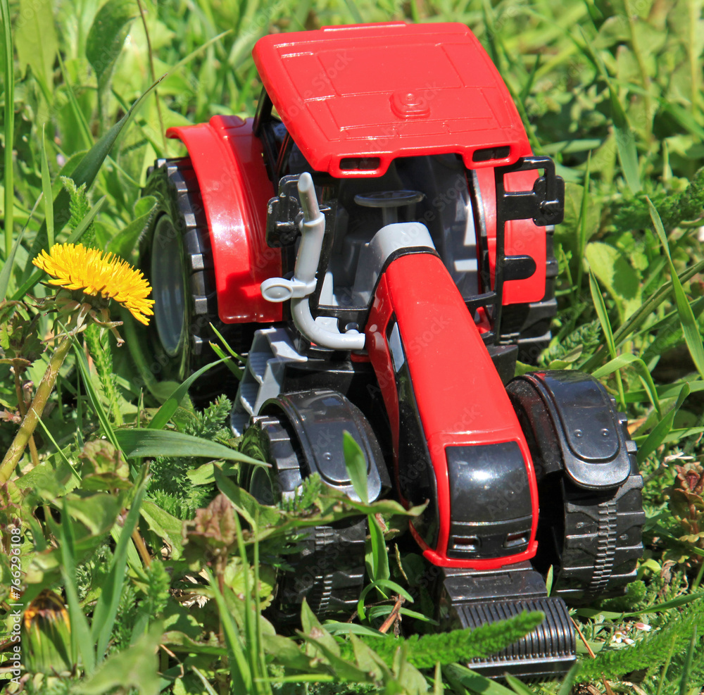 Red tractor in the high green grass in early spring. Spring agricultural works. Planting cereals. Agrarian tractor on the green background. Top view of tractor model. Sowing time in the village Red tractor in the high green grass in early spring. Spring agricultural works. Planting cereals. Agrarian tractor on the green background. Top view of tractor model. Sowing time in the village