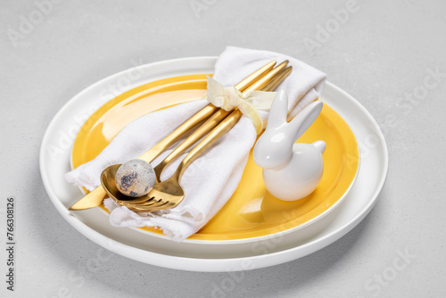 Yellow white plates, white napkin, gold cutlery and quail egg, ceramic bunny on them. Easter table.