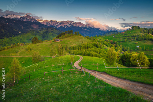 Winding rural road on the green meadow at sunset