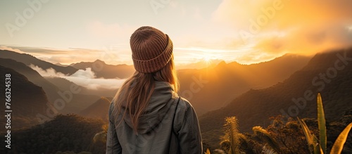 A thoughtful woman standing on the mountain top  staring at the captivating sunset view with the mountains in the background
