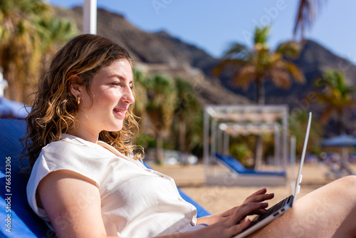 woman is sitting on a blue beach chair with a laptop in front of her