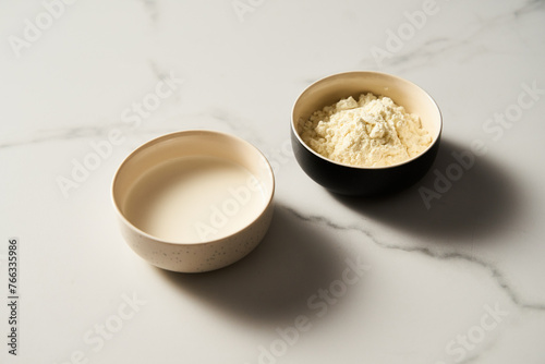 Dry powdered milk and usual milk in the bowl on white marble background  Minimalistic food photo.