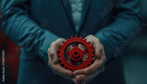 Man holding a red gear in hands - Close-up of a man in a blue suit holding a red gear symbolizing control, mechanics, and interconnectivity