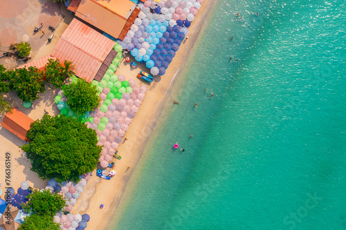 Aerial view view of the beach with umbrellas and bathing people, inflatable rings and boats, clear azure water
