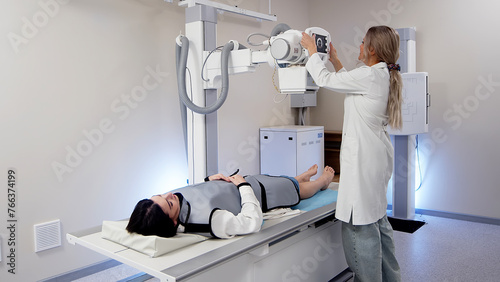 Photos A specialist doctor in an X-ray room, a radiologist sets up a machine for radiography of a patient and makes a scan