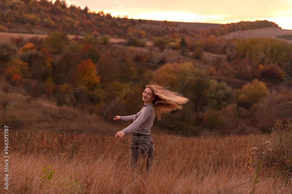 Young attractive blonde woman standing on the hill at sunset