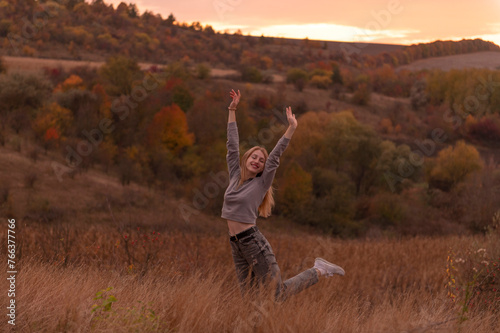 Young attractive blonde woman standing on the hill at sunset