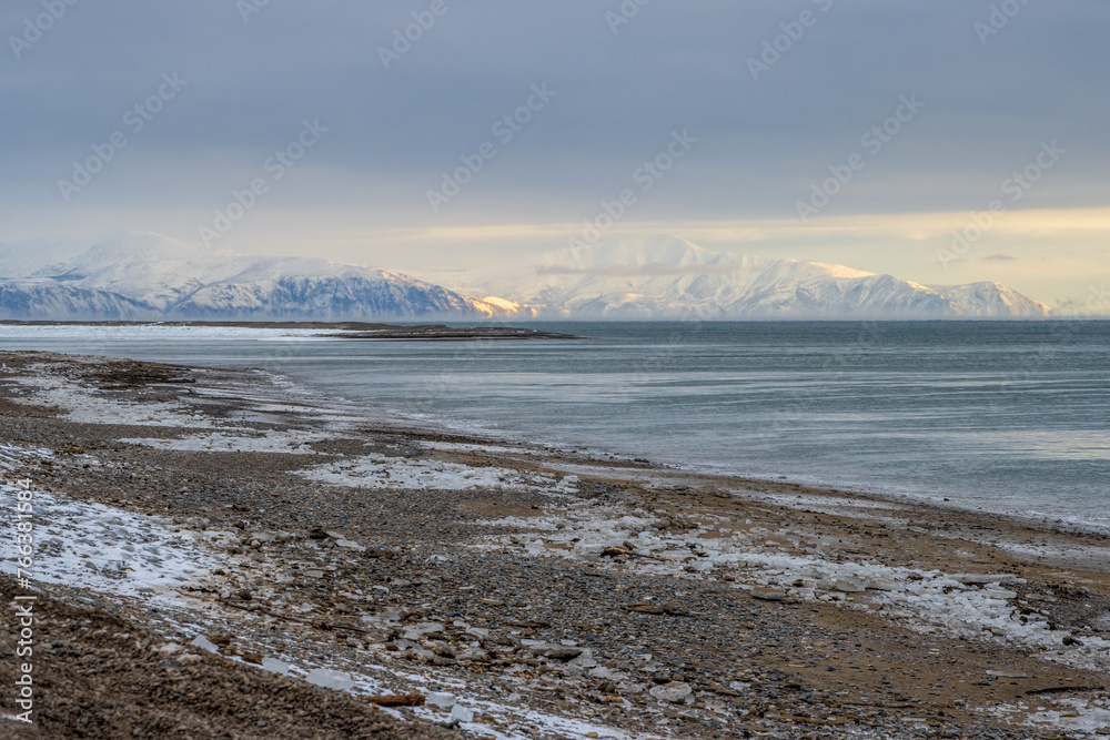 Winter seascape. View of the icy seashore. Mountains in the distance. Cold frosty winter weather. Sea of Okhotsk, Magadan region, Russian Far East.