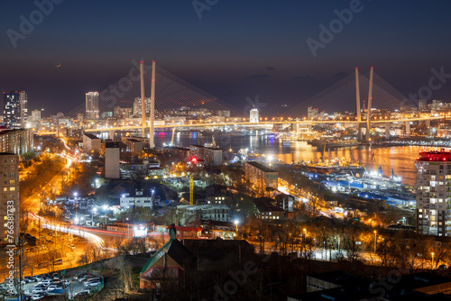Beautiful night city landscape. Top view of streets and buildings. In the distance is a large cable-stayed Golden Bridge over the Golden Horn Bay. Vladivostok city, Primorsky Krai, Russian Far East. © Andrei Stepanov