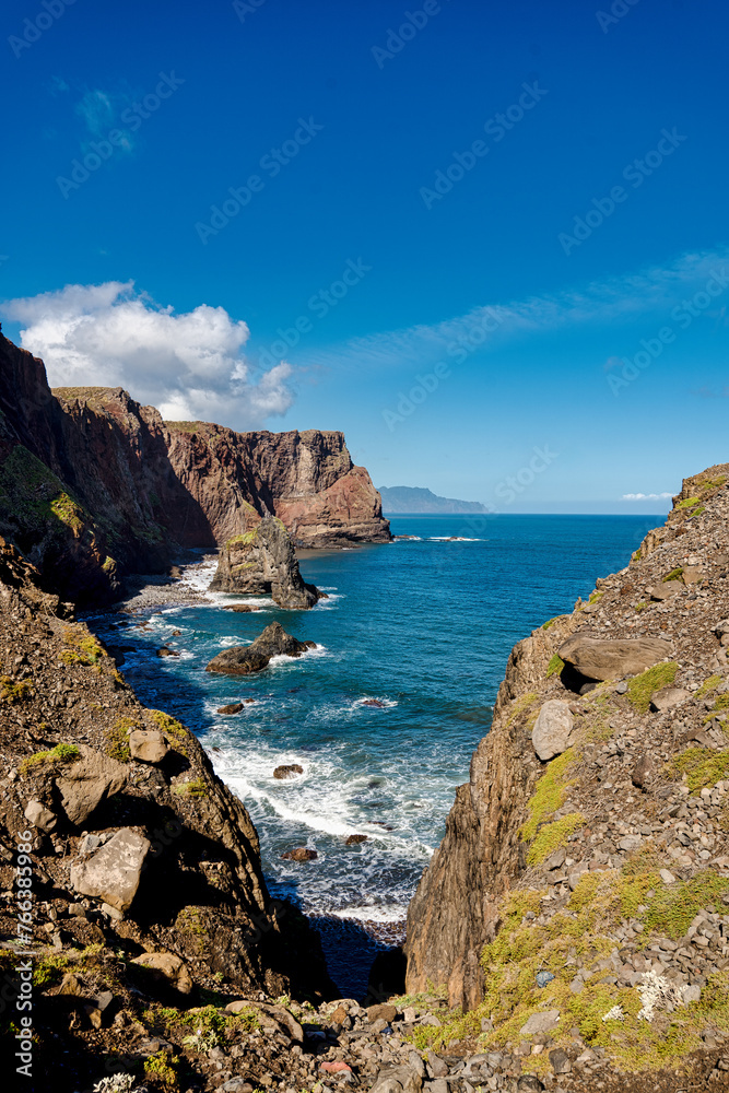 The picture showcases a picturesque rocky coastline with a dominant, tall rock rising from the azure waters of the ocean, under a clear sky. It's a scene full of tranquility and the majesty of nature.