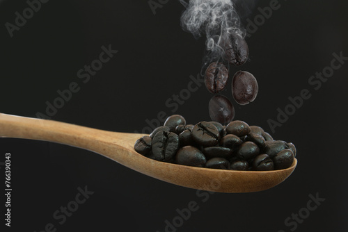 Coffee beans roasted dark on a wooden spoon, with a black background
